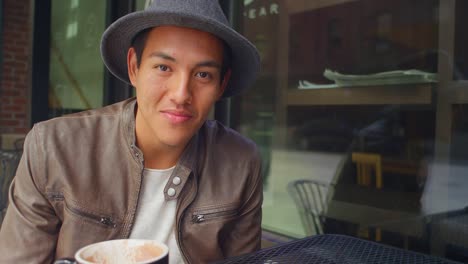 Young-man-sitting-outside-a-coffee-shop-talks-and-smiles-smiles,-portrait