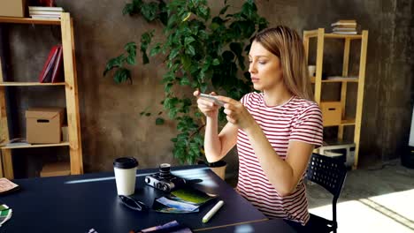 Junge-Frau-ist-die-Anordnung-Bilder,-Take-out-Kaffee,-Sonnenbrille,-professionelle-Kamera-und-Marker-auf-Tisch-und-schießen-flach-legen-mit-Smartphone,-dann-Check-Fotos