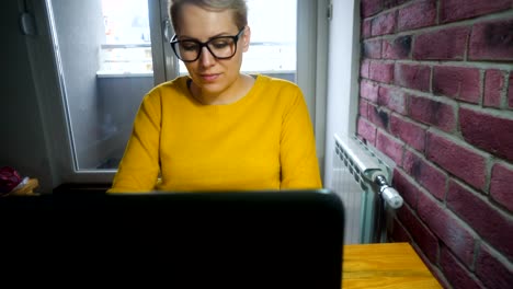 Attractive-young-woman-working-at-the-desk-with-a-laptop-in-home-office.