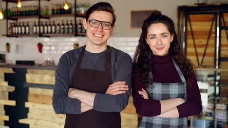 Portrait-of-two-coffee-house-owners-attractive-young-people-standing-inside-coffee-shop,-smiling-and-looking-at-camera.-Successful-start-up-and-beautiful-people-concept.
