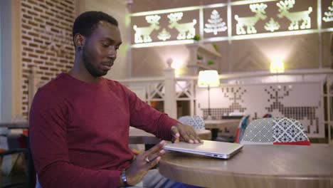 Portrait-of-happy-african-businessman-sitting-in-a-cafe-and-working-on-laptop