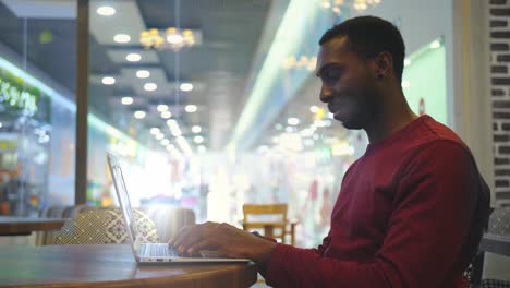 Portrait-of-happy-african-businessman-sitting-in-a-cafe-and-working-on-laptop