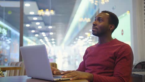 Portrait-of-happy-african-businessman-sitting-in-a-cafe-and-working-on-laptop