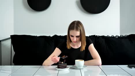 Young-beautiful-women-with-heavy-make-up-eating-cake-and-sitting-on-sofa,-black-and-white-cafe-background