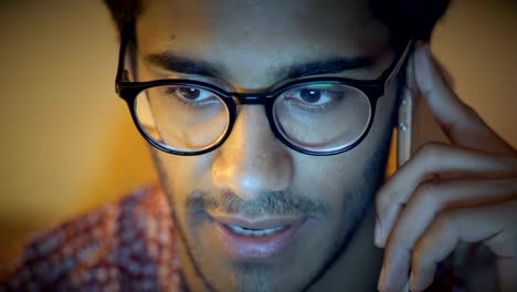 Close-up,-Indian-Man-In-Glasses-Speaks-On-Phone-Sitting-Behind-Computer,-Discussing-Business-Questions