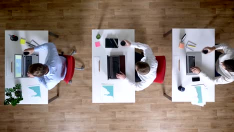 Three-young-businessman-are-working-on-laptops,-drink-coffee-simultaneously,-work-concept,-office-concept,-communication-concept,-top-shot