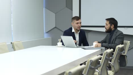 Male-Colleagues-Drinking-Coffee-and-Using-Laptop-in-Meeting-Room