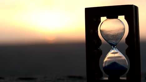 Hourglass-Passing-of-Time-Lapse-Clouds.-An-hourglass-in-front-of-a-bright-blue-sky-with-puffy-white-clouds-passing.-Time-concept.-Sunset-time.-Selective-focus