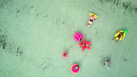 Aerial-view-of-friends-floating-on-inflatable-mattresses-in-transparent-sea.