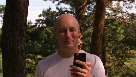 Adult-man-talking-by-video-cal-in-mobile-phone-while-travel-in-summer-forest