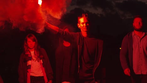 Grupo-de-adolescentes-graves-con-una-celebración-y-agitando-rojo-señal-Flare-caminando-hacia-adelante-hacia-la-cámara-en-la-noche.