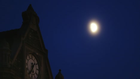 Gruselige-Turmuhr-mit-Mond-auf-dem-klaren,-blauen-Himmel