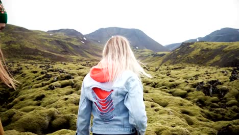 Back-view-of-two-tourists-woman-hiking-together-in-Iceland.-Girls-walking-through-the-lava-field-covered-moss