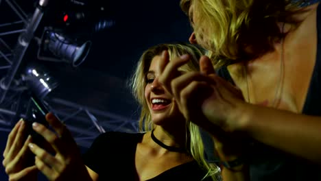 Female-friends-reviewing-pictures-on-mobile-phone-at-a-concert-4k