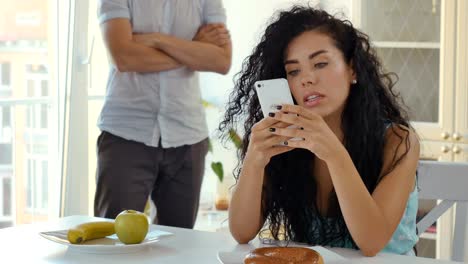 Woman-uses-phone-sitting-at-table,-funny-man-squats-at-the-background