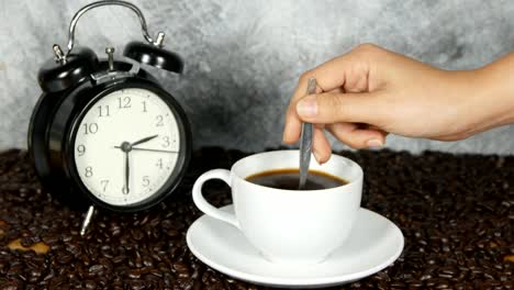 4k-of-Close-Up-Female-Hand-Stirring-Cup-Black-Coffee---female-hand-using-spoon-to-stir-freshly-brewed-ground-black-coffee-white-cup-saucer-beside-whole-coffee-beans,-Coffee-time