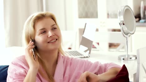 Mujer-joven-en-conversaciones-domésticas-albornoz-teléfono-sentado-en-el-sofá-en-la-sala-de-estar