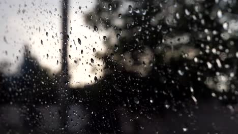 Close-up-of-raindrops-on-car-window-during-bad-weather-with-blur-background.-Water-droplets-fall-on-the-glass-of-automobile-during-drive-at-countryside.-POV-Slow-motion