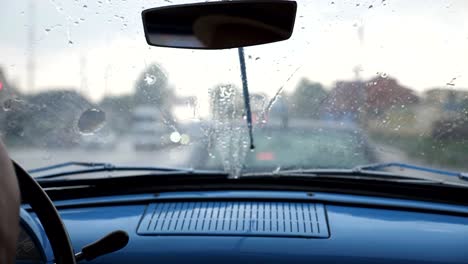 POV-from-the-front-seat-to-windshield-of-old-retro-car-during-bad-weather.-Wipers-removing-raindrops-from-the-window-of-vintage-automobile-during-standing-in-traffic-jam.-Close-up-Slow-motion