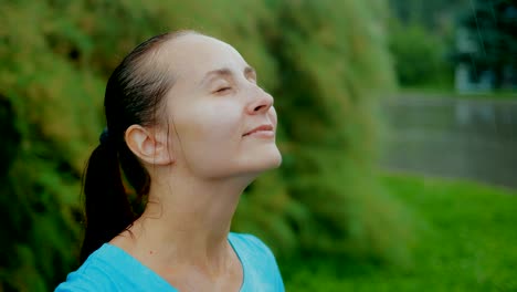 Porträt-einer-Frau-mit-geschlossenen-Augen-in-der-Regen-in-der-Natur-mit-nassen-Haaren-und-wischt-sich-sein-Gesicht-in-seinen-Händen