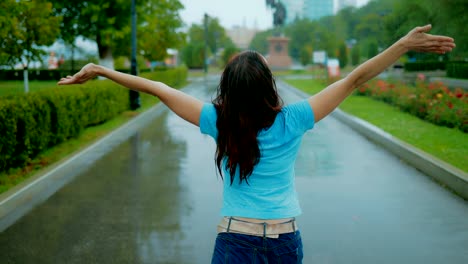 Glückliche-und-schöne-rothaarige-Frau-zu-Fuß-im-Park-unter-den-strömenden-Sommer-Rainю-Ansicht-von-hinten