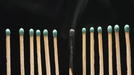 SLOW-MOTION:-Smoke-of-single-burned-matchstick-between-row-of-new-matchsticks