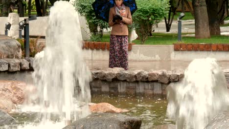 A-beautiful-girl-with-sad-eyes-is-standing-in-the-rain-in-the-city-park,-near-the-fountain.