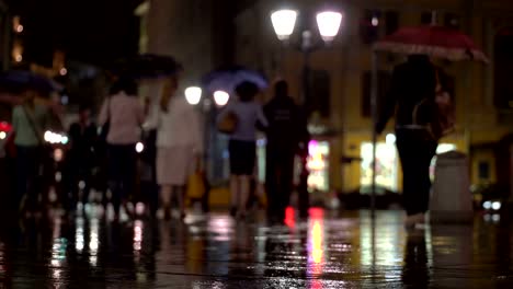 Zusammenfassung-Hintergrund-regnerischen-späten-Abend-in-der-Stadt-in-dunklen-Tönen-Naturale.-Regentropfen-fallen-auf-dem-bunten-Asphalt-von-Straßenlaternen-beleuchtet.-Unter-der-Menge-von-Fußgängern-gehen-Sie-zwei-Freunde-unter-Sonnenschirmen-und-sprechen.-Lebensstil-der-modernen-Stadt