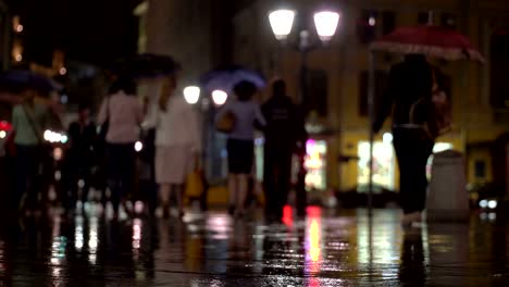 Resumen-tarde-lluviosa-de-fondo-en-la-ciudad-en-tonos-oscuros-naturale.-Las-gotas-de-lluvia-caen-sobre-el-asfalto-colorido,-iluminado-por-farolas.-Entre-la-multitud-de-peatones-van-a-dos-amigos-bajo-paraguas-y-hablar.-Estilo-de-vida-de-la-ciudad-moderna