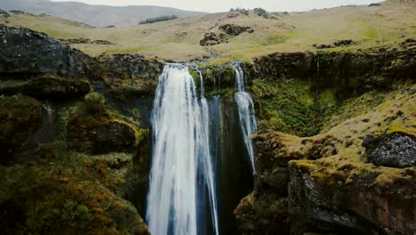 Aerial-view-of-the-waterfall-Gljufrabui-in-Iceland.-Copter-moves-down,-group-of-people-standing-on-the-top-of-mountain