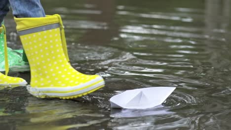 Niños-de-botas-de-goma,-jugando-con-barcos-de-papel