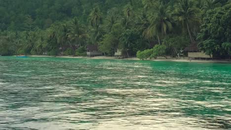 Tropical-rain-over-the-bamboo-homestay-huts-on-the-beach,-Gam-Island,-Raja-Ampat,-West-Papua,-Indonesia