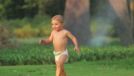 Schöne-realen-Moment-der-Säugling-Baby-Boy-Laufzeit-in-Zeitlupe-60fps-im-grünen-Feld-mit-Wasser-Sprinkes-auf-Sommer-Sonnenuntergang-goldene-Stunde-in-4-k-Clip-Auflösung