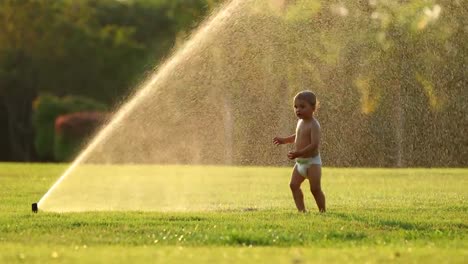 Infant-baby-running-with-water-sprinkles-in-outdoor-garden-during-sunset-golden-hour-time-in-4K.-Idealic-scene-of-happy-infant-baby-enjoying-the-simple-things-in-life