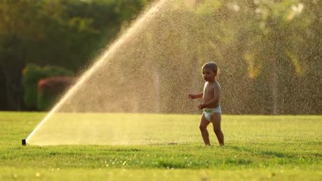 Säugling-Baby-läuft-mit-Wasser-besprengt-im-Garten-während-des-Sonnenuntergangs-goldene-Stunde-Zeit-in-4K.-Idyllischen-Szene-glücklich-Baby-Babys-genießen-die-einfachen-Dinge-im-Leben