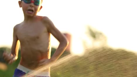 Niños-divirtiéndose-con-chispitas-de-agua-en-cámara-lenta-60fps-4k-clip-resolución.-Joven-por-sí-mismo-jugando-afuera-en-el-césped-con-agua-y-las-cosas-simples-de-la-vida