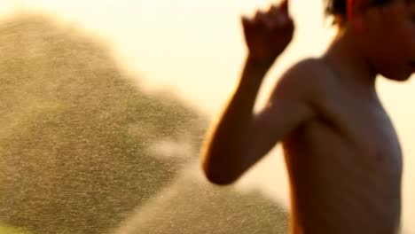 Children-having-fun-outside-with-water-sprinkles-during-sunset-time.-4k-clip-of-children-enjoying-their-summer-vacations-outside-with-water-sprinkles-4K