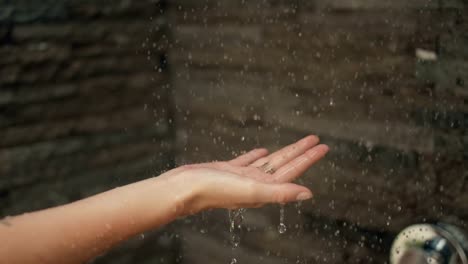 In-der-Dusche-Frau-legt-ihre-Hand-unter-Strom-des-Wassers.-Tröpfchen-landen-auf-ihrem-Palm.