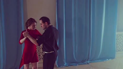 Couple-dancing-tango-in-the-studio.-Young-woman-in-a-red-dress-and-a-man-doing-professional-movements-while-dancing-tango.-Slow-motion