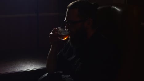 Young-bearded-man-in-glasses-drinks-tea-in-hookah-lounge-room-closeup-on-black-background-in-slow-motion-in-4k