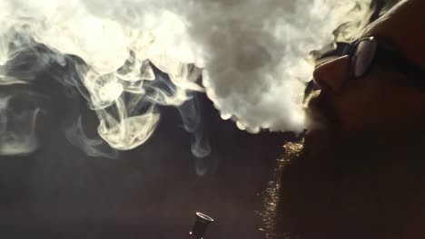 young-bearded-man-in-glasses-smokes-a-hookah-and-blow-out-smoke-closeup-on-black-background-in-slow-motion-in-4k