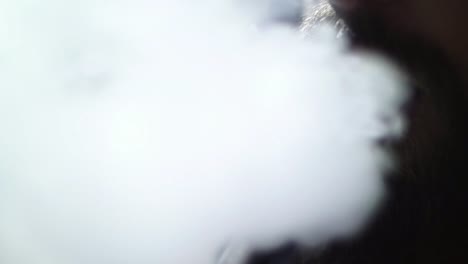 hombre-barbudo-joven-en-gafas-fuma-un-narguile-y-sople-closeup-humo-sobre-fondo-negro-en-cámara-lenta-en-4k