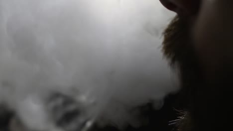 young-bearded-man-in-glasses-smokes-a-hookah-and-blow-out-smoke-closeup-on-black-background-in-slow-motion-in-4k