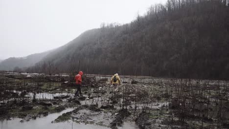 man-and-him-friends-in-autumn-jackets-trying-to-cross-the-swamp-in-the-rain