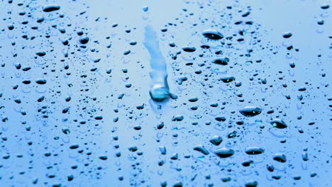 Rain-droplets-or-water-droplets-flowing-on-glass-on-sunlight-daytime.-Closeup-rain-falling-to-splash-on-bright-surface-of-mirror-of-car-background