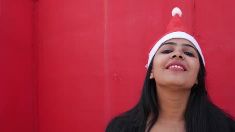 Close-up-portrait-of-young-Indian-girl-with-Santa's-hat-making-faces-towards-the-camera,-excited-and-extremely-happy