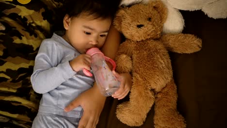 Asiatische-Mädchen-essen-Milch-mit-einer-Flasche,-halten-Teddybär