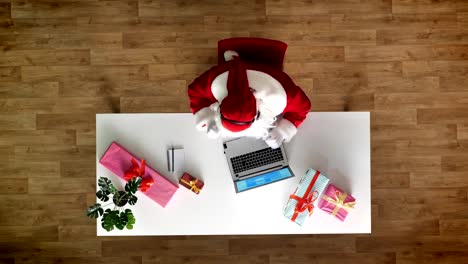 Santa-Claus-arbeiten-im-Büro-am-Laptop,-Musik-hören,-Kopfhörer,-schreibt-Typisierung,-aerial-Blick,-von-oben-nach-unten-geschossen,-Text-in-ein-Notizbuch