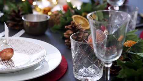 Panorámica-cerca-encima-de-adornos-de-Navidad-en-placas-sobre-una-mesa-decorada-para-cena-de-Navidad,-enfoque-selectivo