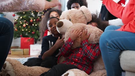 Kinder-spielen-mit-riesigen-Teddybär-als-mehr-Generationen-Familie-öffnen-Geschenke-am-ersten-Weihnachtstag